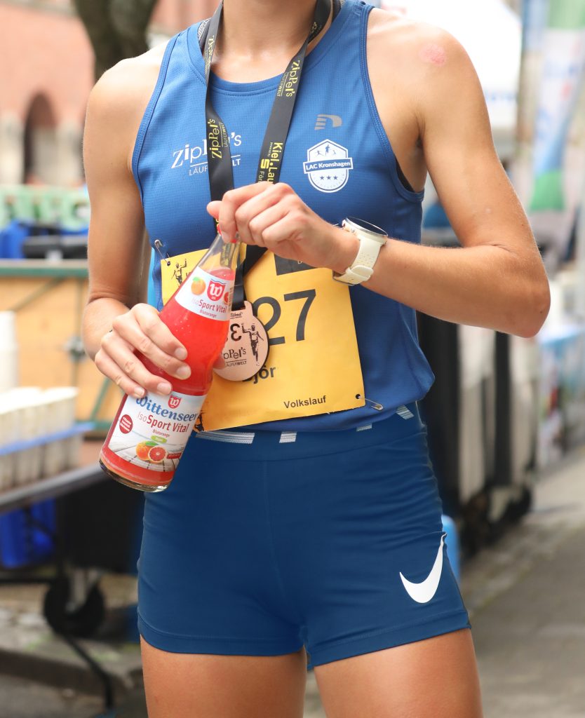 Marathonläuferin hält Wittenseer IsoSport Vital Blutorange Glas-Mehrweg in der Hand.